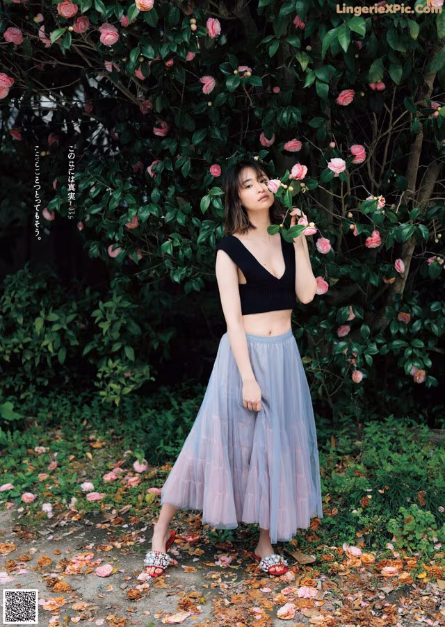 A woman standing in front of a bush of flowers.