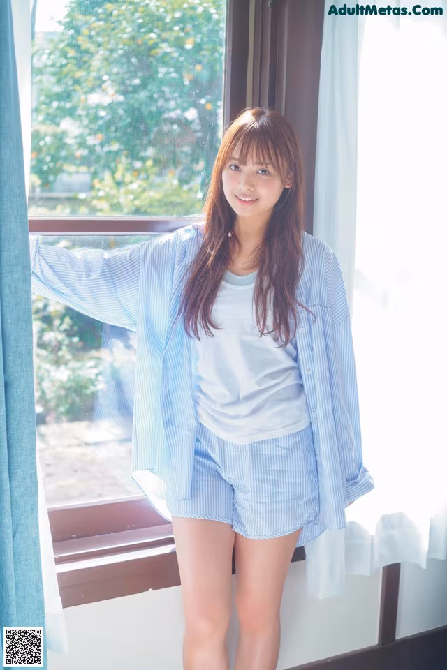 A woman standing in front of a window wearing a blue and white striped shirt.