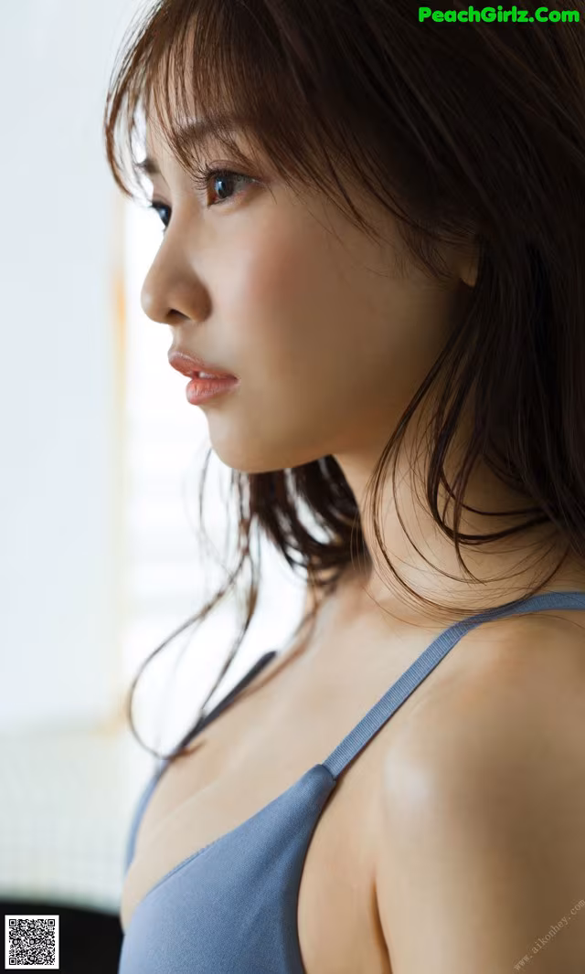A woman in a blue bra top looking out a window.