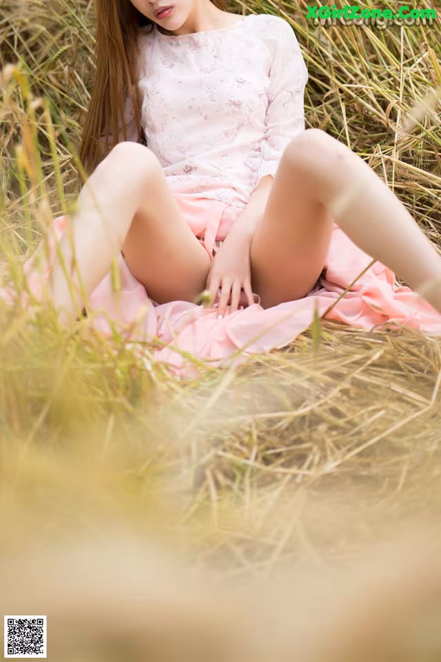 A woman in a pink dress sitting in a field of tall grass.