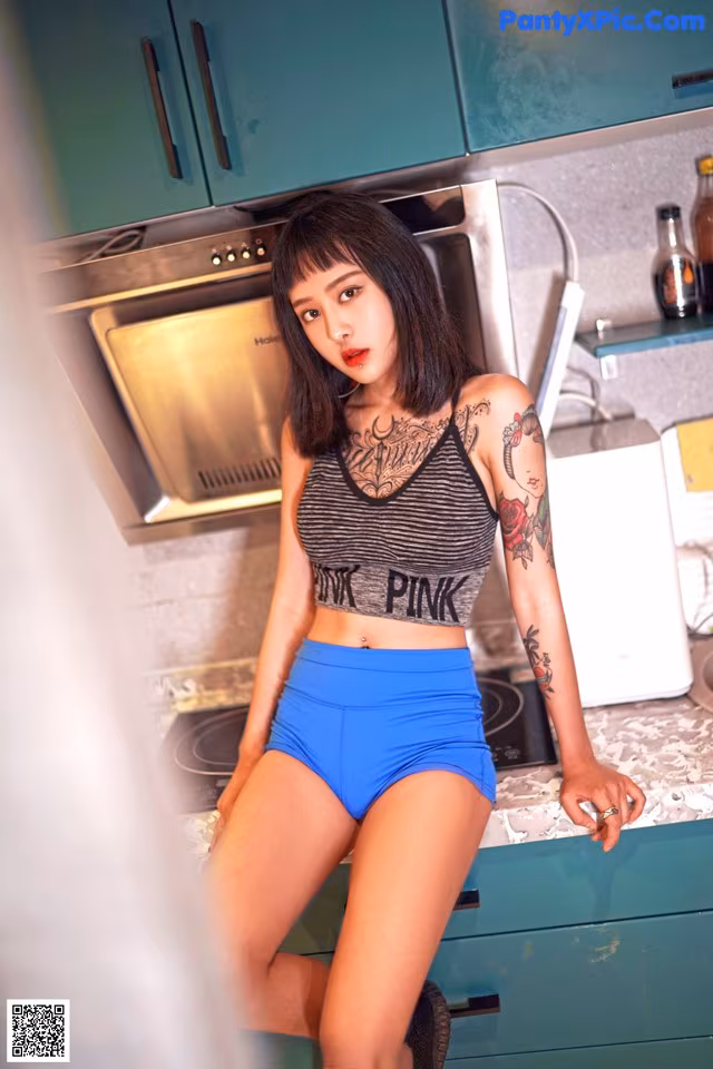 A woman in a black and white top and blue shorts posing in a kitchen.