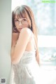 A woman in a white dress leaning against a wall.