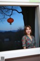 A woman standing in front of a window with a red lantern.