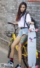 A woman standing next to a yellow bike holding a skateboard.