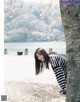 A woman leaning against a tree in front of a lake.