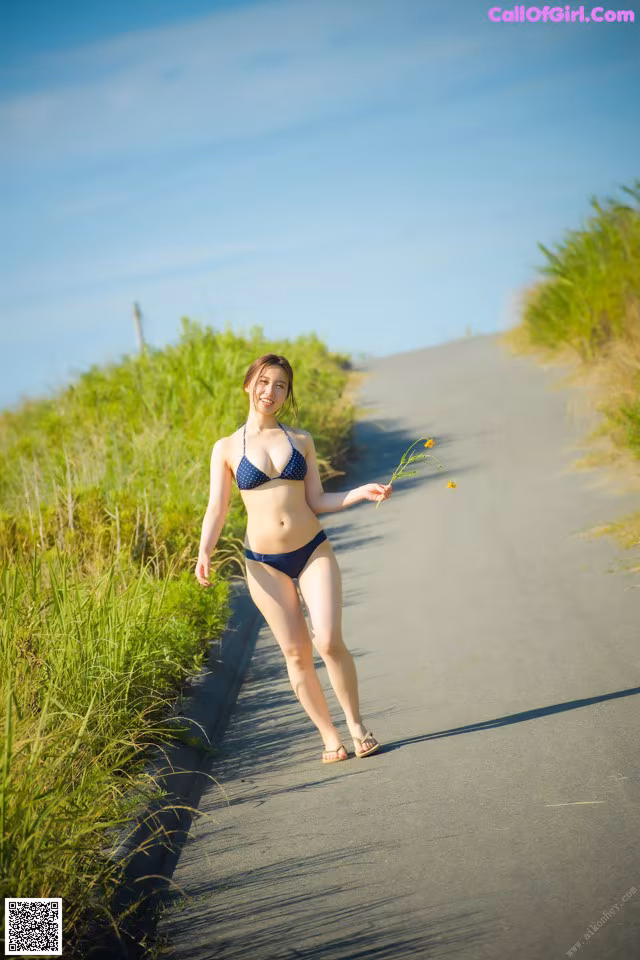 A woman in a bikini walking down a road holding a flower.