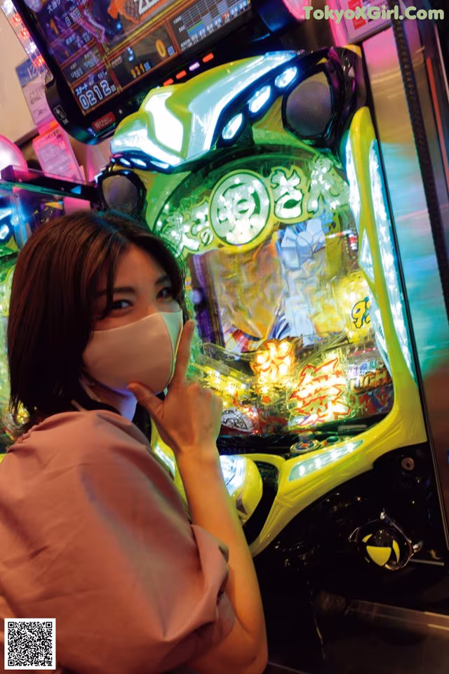 A woman wearing a face mask in front of a slot machine.