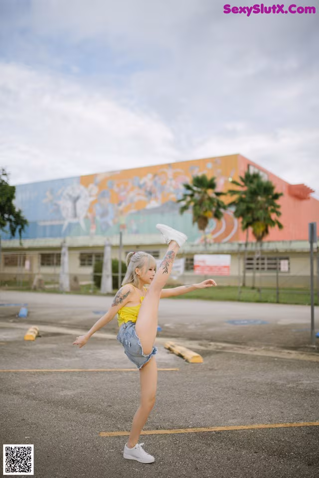 A woman in a yellow tank top and denim shorts doing a handstand.