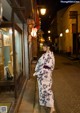 A woman in a kimono walking down a street at night.