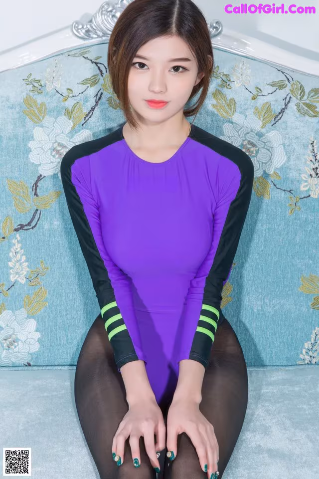 A woman in a purple and black bodysuit sitting on a blue couch.